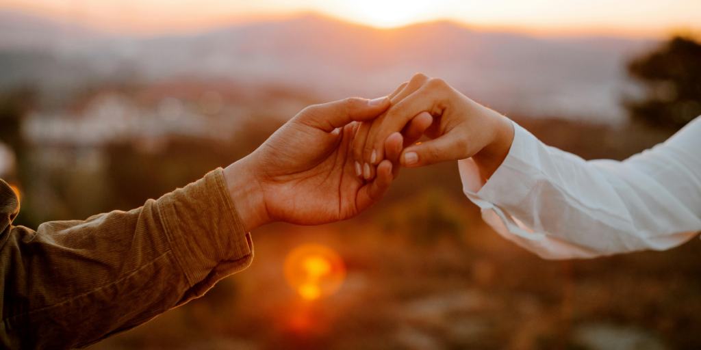 Two people holding hands with a mountain sunset in the background