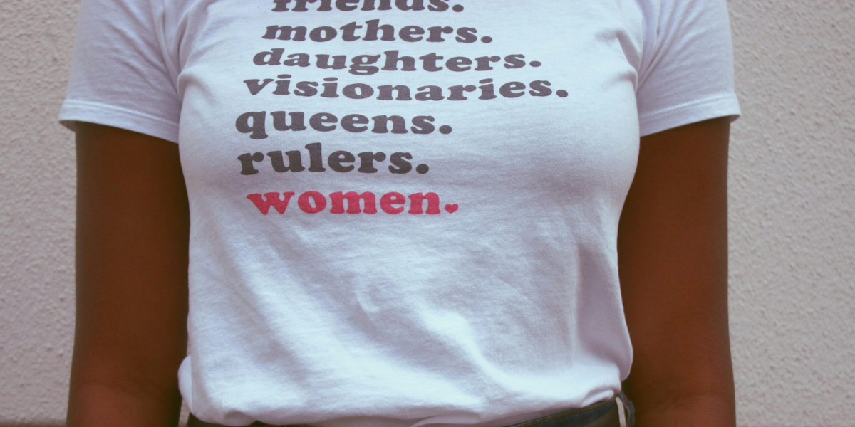 Woman wearing a t-shirt with the printed words "friends, mothers, daughters, visionaries, queens, rulers, women"