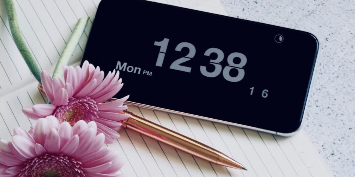 Digital alarm clock with time 12:38 PM with pink flowers in the foreground