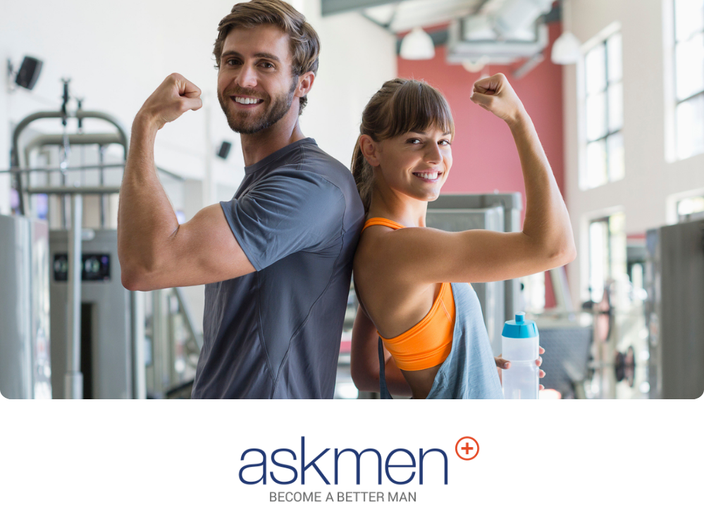 Stock image of a man and a woman standing back to back showing off their arm muscles inside a gym.