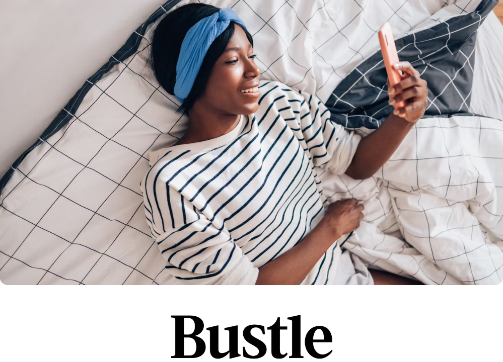 Stock image of a woman laying in bed looking at her phone, seemingly on FaceTime.