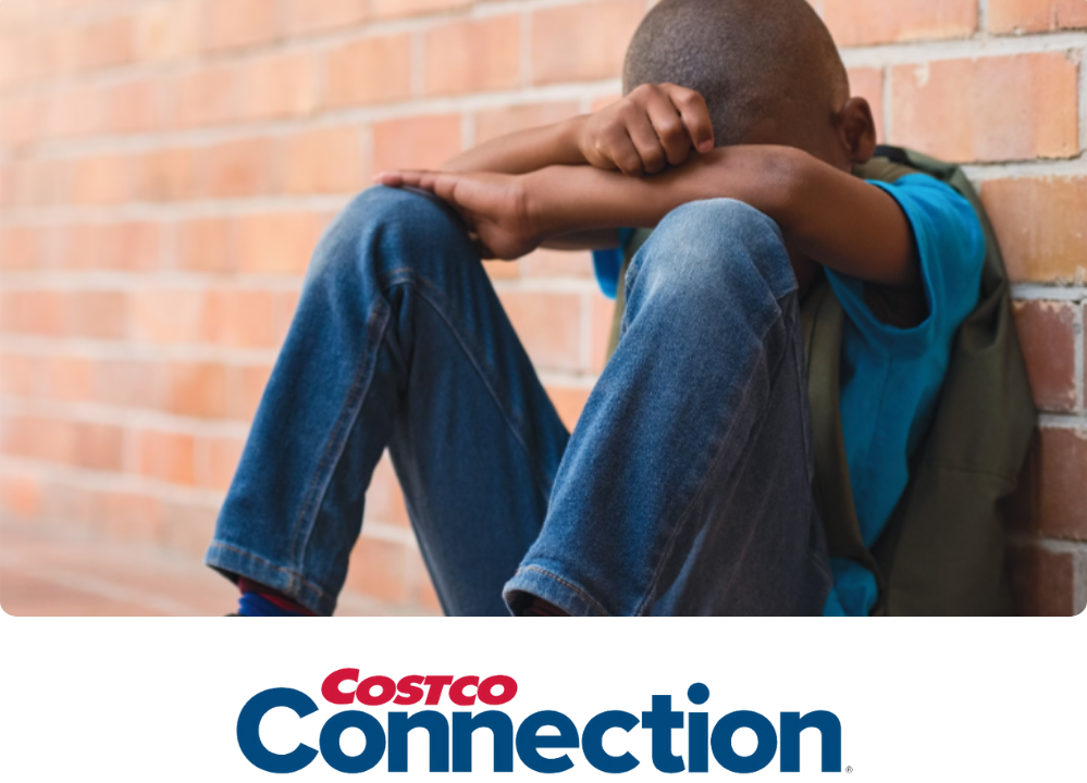 Stock image of a little boy sitting against a brick wall with his hands and head on his knees, looking seemingly upset.