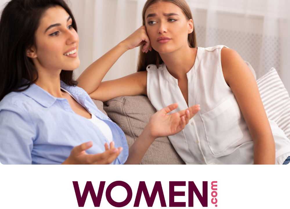 Stock image of two women sitting on a couch, one looking at the other with their eyebrow raised.