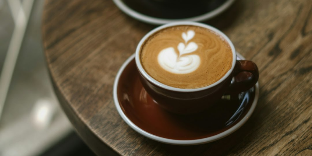 Brown coffee cup sitting on a table with a heart latte design on the coffee.