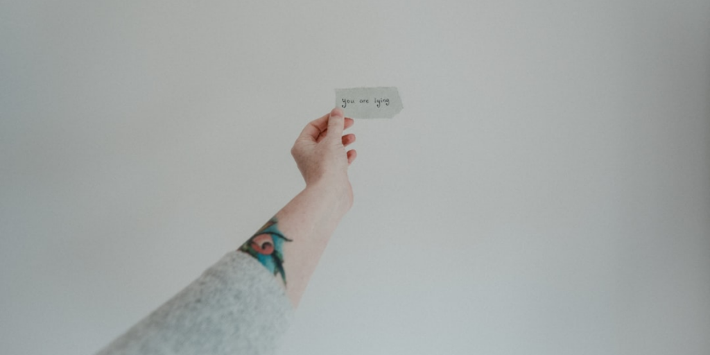 A hand holding out a piece of paper that says "you are lying" on it.