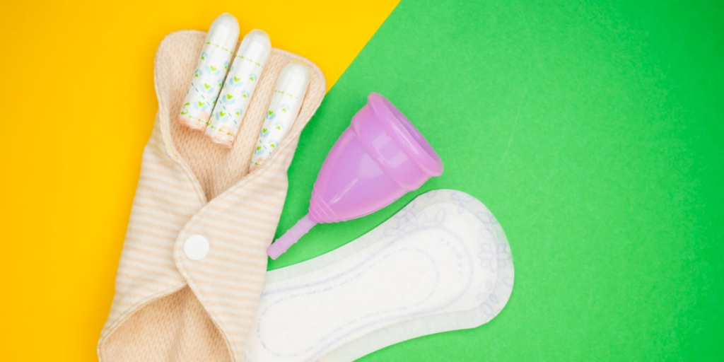 Stock image of tampons, a pad, and a menstrual cup laying next to each other.