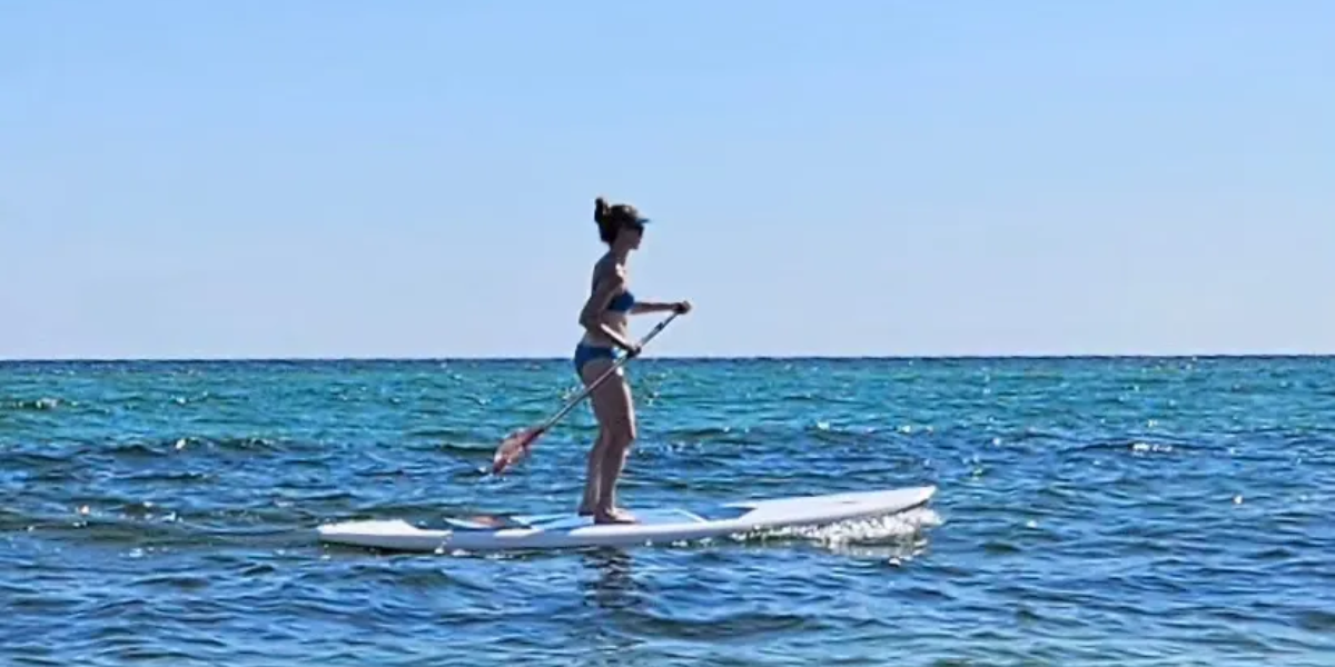 Author Deborah Vinall paddle boarding on the open ocean on a sunny day.