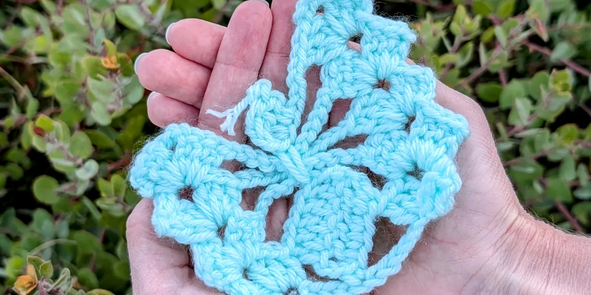 Hands cupped together holding a blue crochet butterfly.