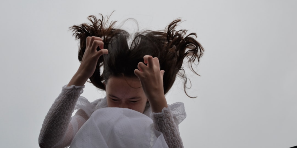 A girl whose hair is sticking up is clenching her hands in emotion.