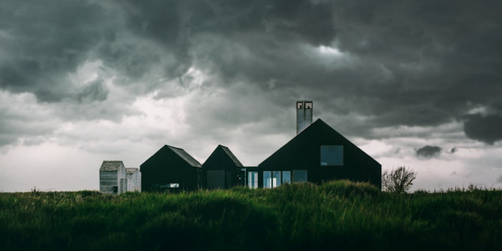 House on the grass with dark clouds overhead.