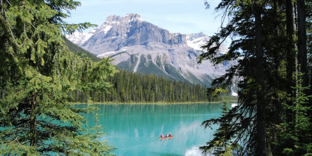 A photo from Banff, Canada with a kayak on a lake surrounded by trees and mountains.
