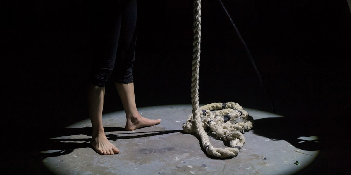 A dark room where a spotlight is on a hanging rope and someone's bare feet.