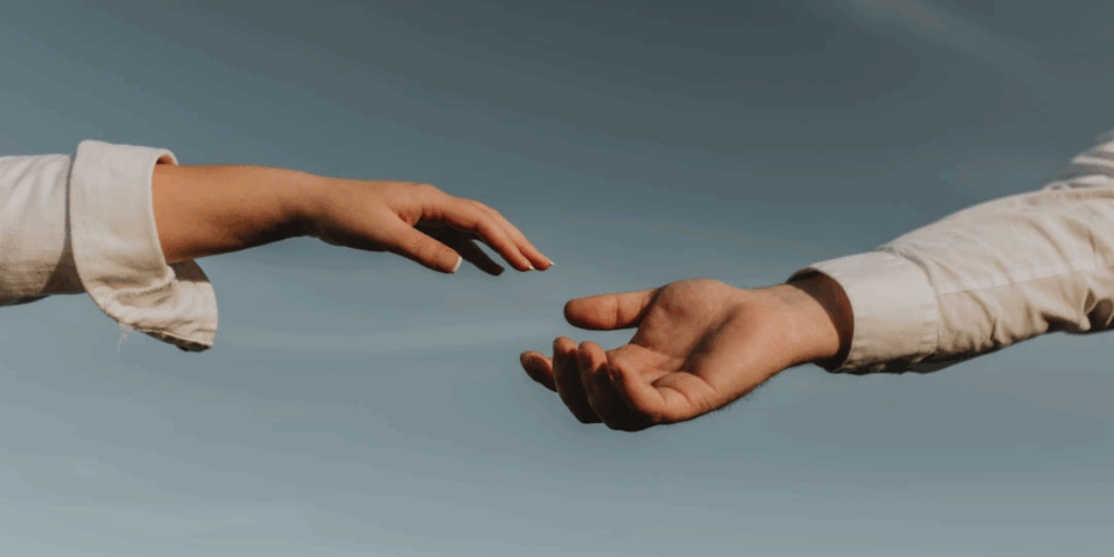 One hand reaching for another person's hand outside.
