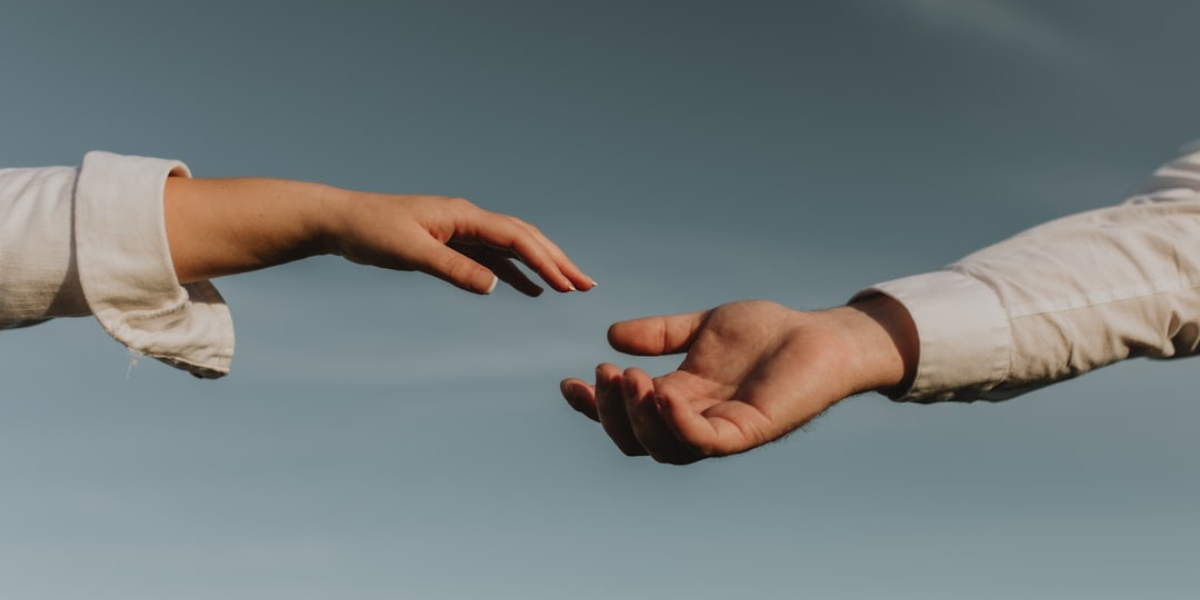 One hand reaching for another person's hand outside.