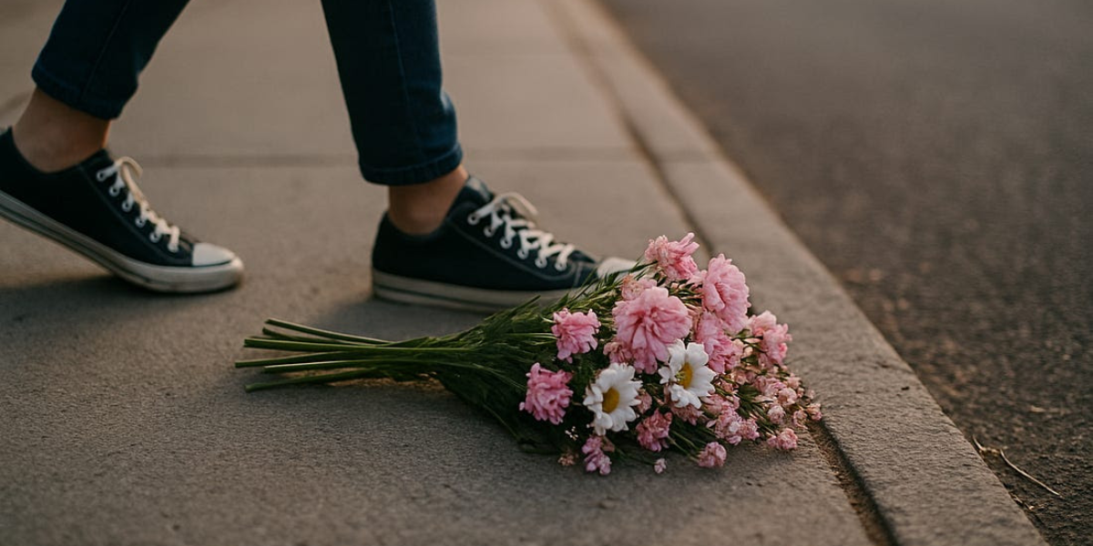 A bouquet of flowers on the ground with someone's feet in converse next to them.