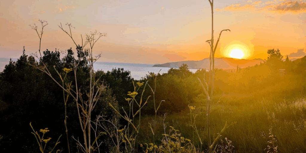 the Croatian coastline north of Dubrovnik with the sun setting behind a hill near the water.