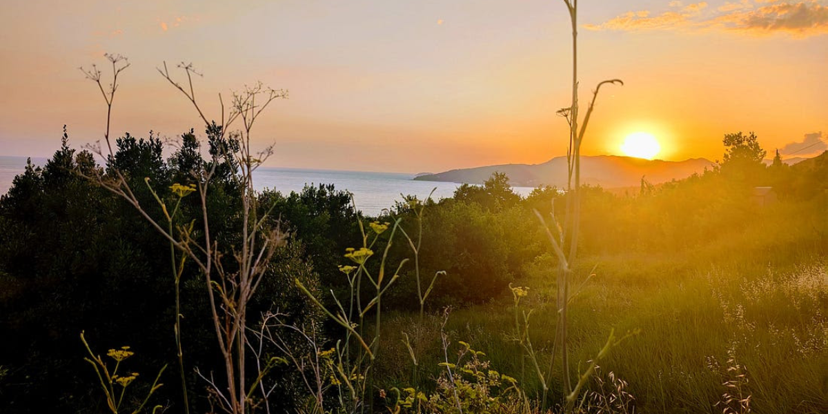 the Croatian coastline north of Dubrovnik with the sun setting behind a hill near the water.