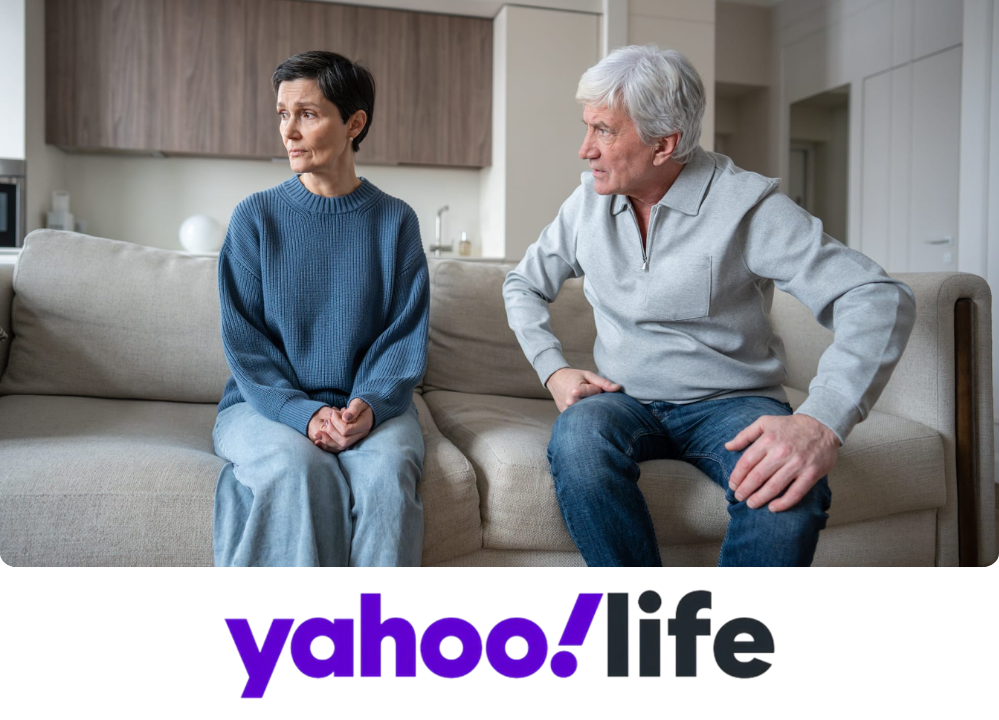 Stock image of a man and woman sitting on a couch, the woman looking away from the man with a concerned look.