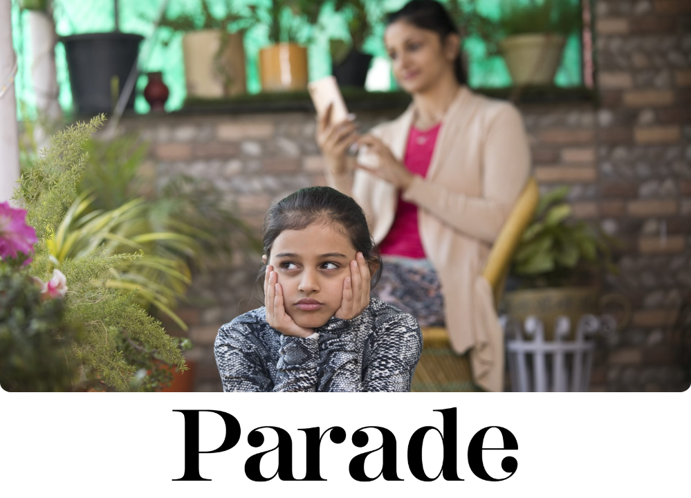 Stock Image of a little girl with her hands under her face, and her mother in the background on her phone and not paying attention to her.