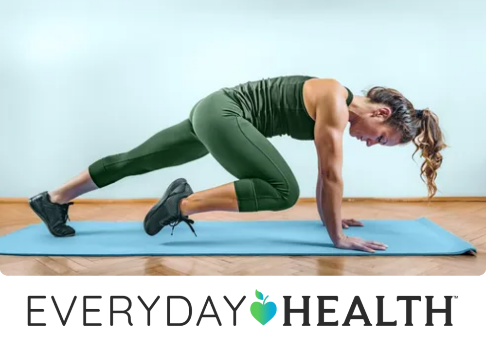 Stock image of a woman in green athletic wear performs a mountain climber exercise on a blue yoga mat.